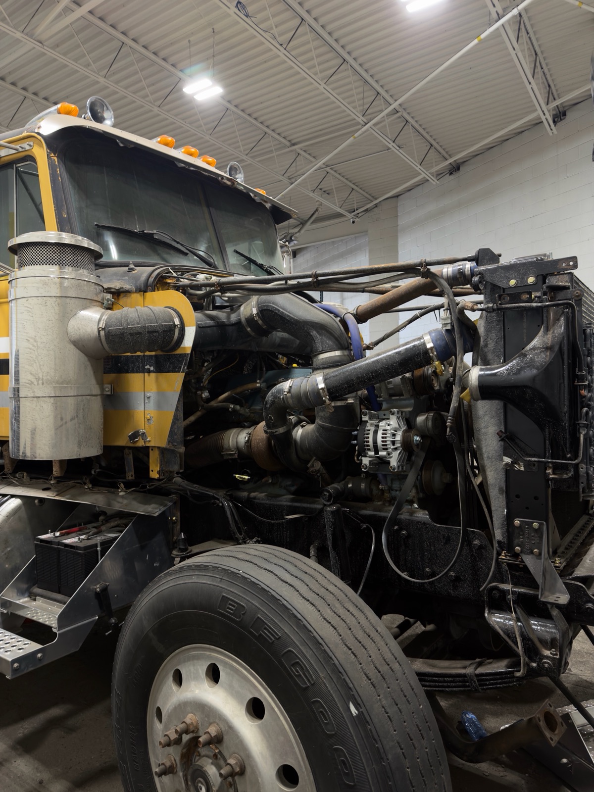 Yellow heavy-duty truck with hood tilted forward exposing the diesel engine during service at the Planet Truck Brampton shop